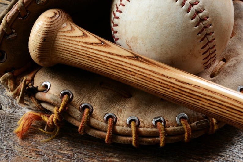 A close up image of an old used baseball, baseball bat, and baseball glove.