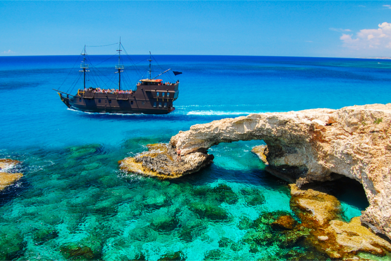 Pirate ship sailing near famous rock arch on Cavo Greko peninsula, Cyprus island