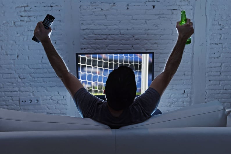 Young man home alone watching soccer or football game in television