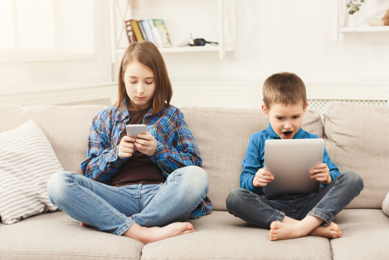 Brother and sister playing online games on smartphone and pad