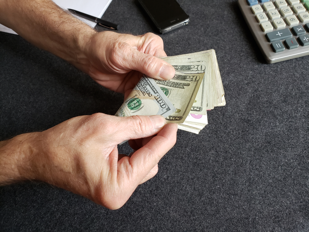 pair of hands holding a bundle of twenty dollar notes