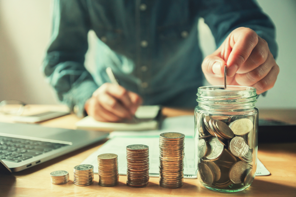 man's hand placing coins in jar while counting money