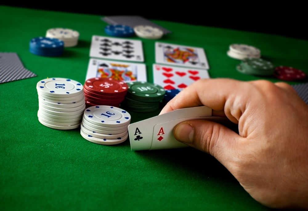 hand-holding-two-aces-cards-on-poker-table-containing-chips-and-cards