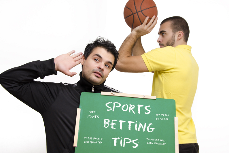 Male holding sports betting tips sign in front of another playing basketball
