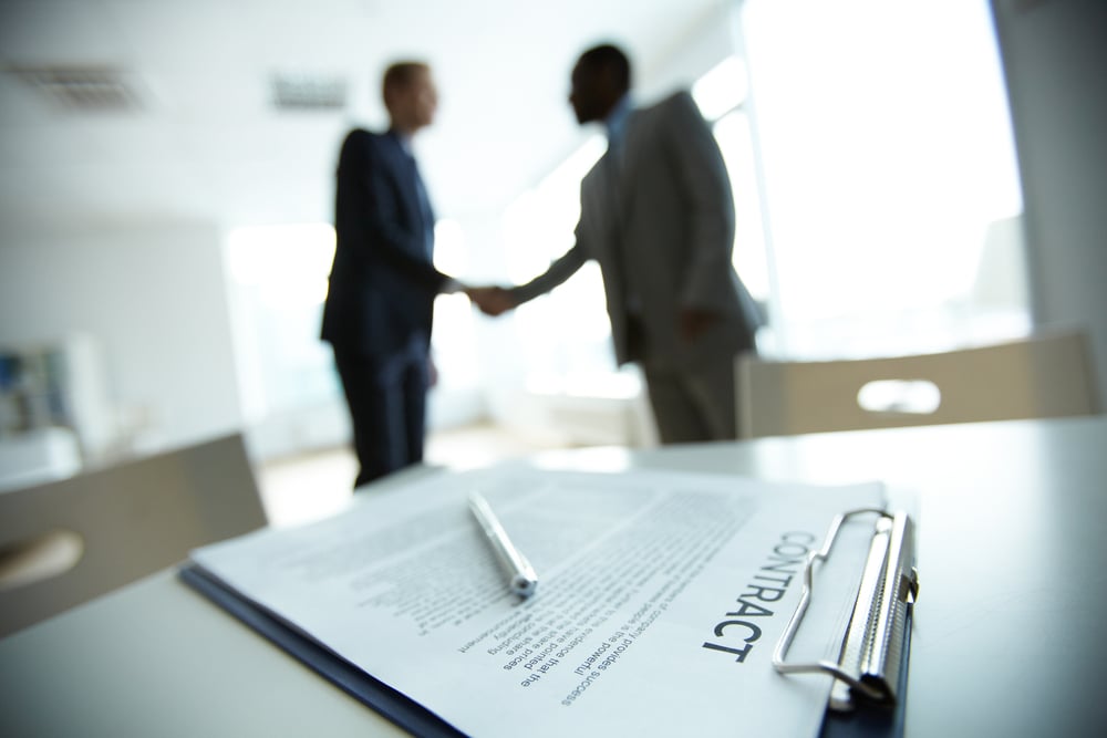 two men in suits shaking hands over contract agreement