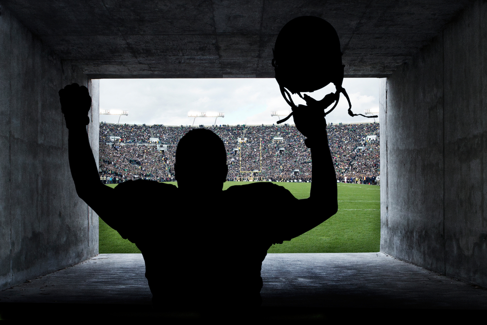 football player holds helmet with arms raised as he's about to enter the football pitch