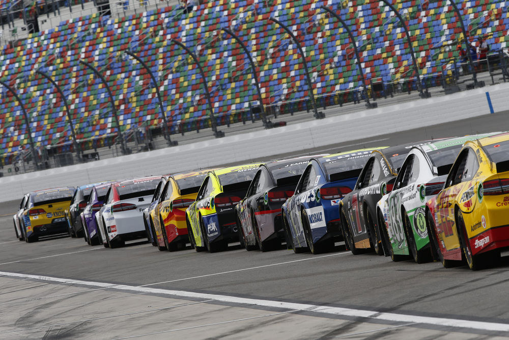NASCAR cars on a racetrack with audience watching on