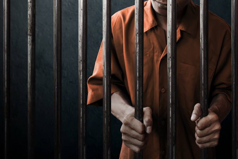 Man holding bars in prison cell.