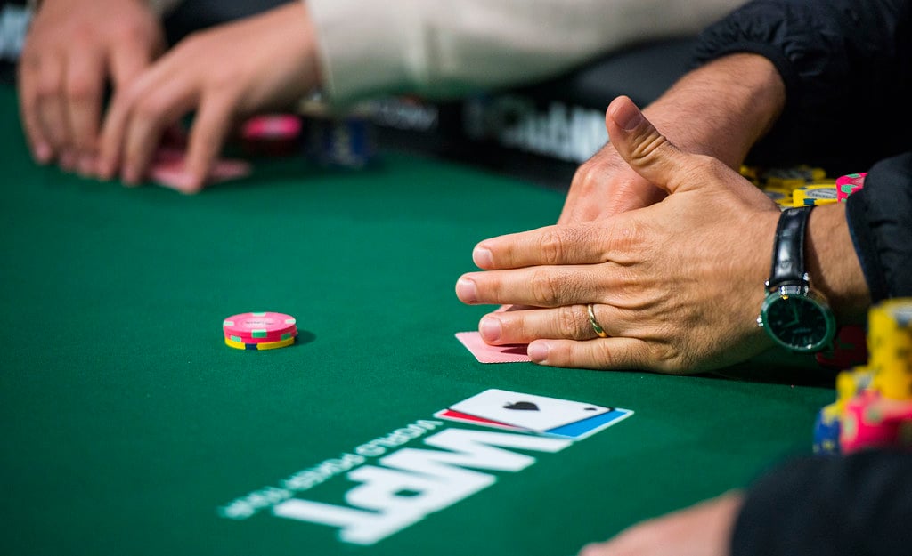 poker players' hands with chips on table with WPT logo