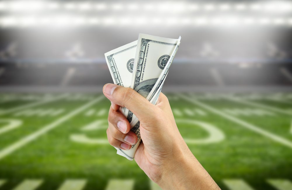 hand holding dollar bills with American football field in the background