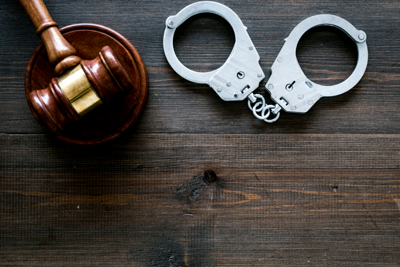 handcuffs near judge gavel on dark wooden desk