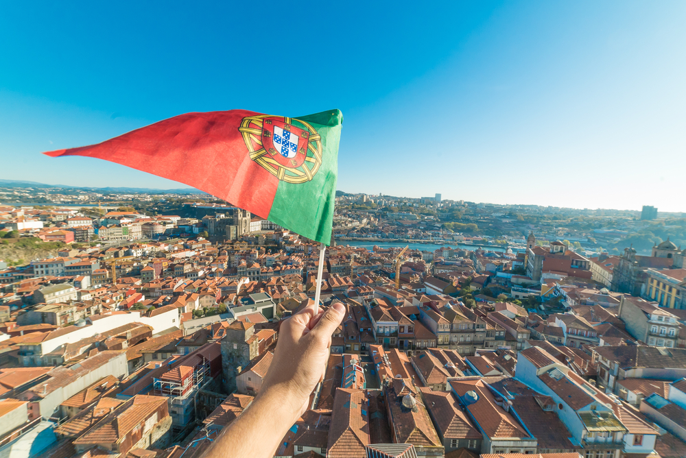 hand holding a flag of Portugal against a city backdrop