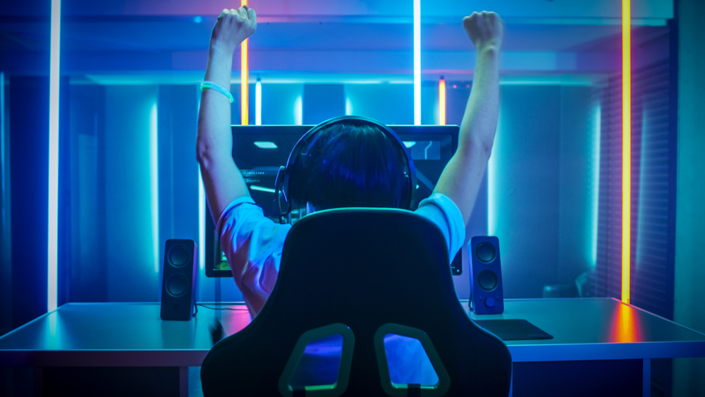 online gamer at desktop computer raises arms in victory