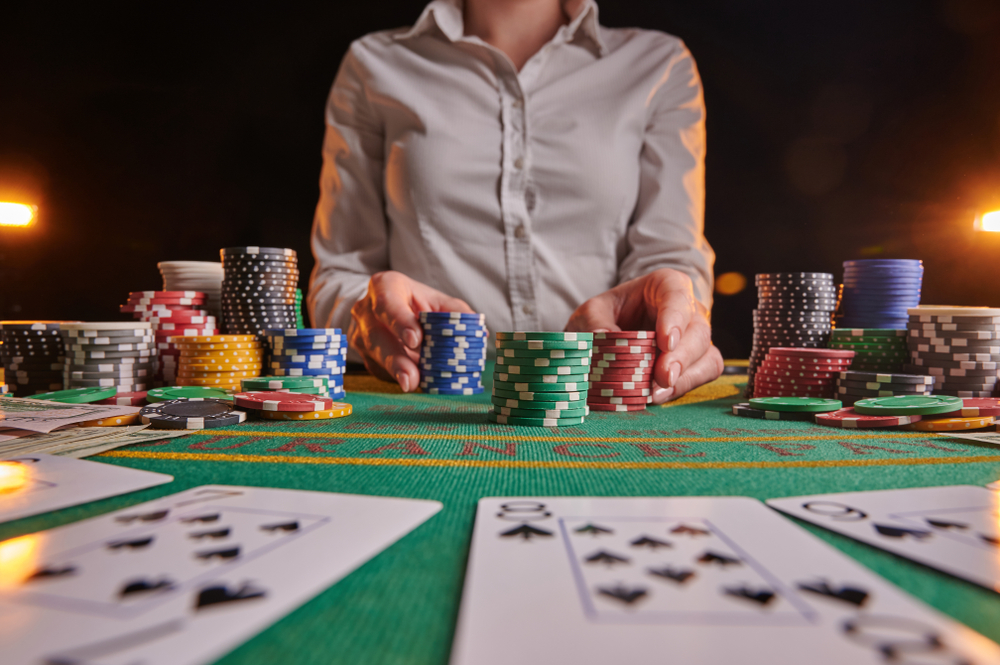 female croupier accepts bets at a casino table laden with cards and chips