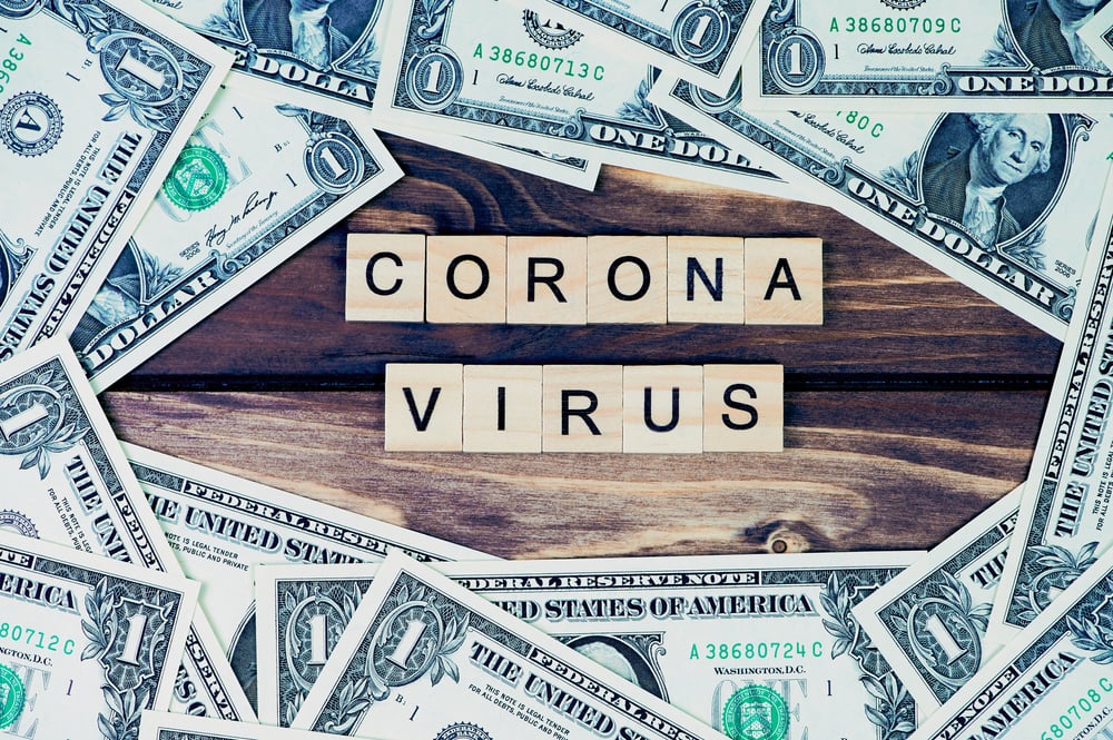 one Dollar bills around the word Coronavirus laid with wooden capital letters as symbol for the financial economic crisis