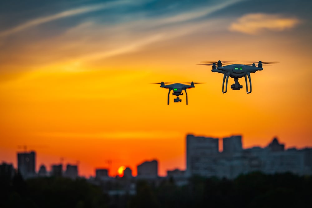 two drones flying against a burnt-orange sunset skyline