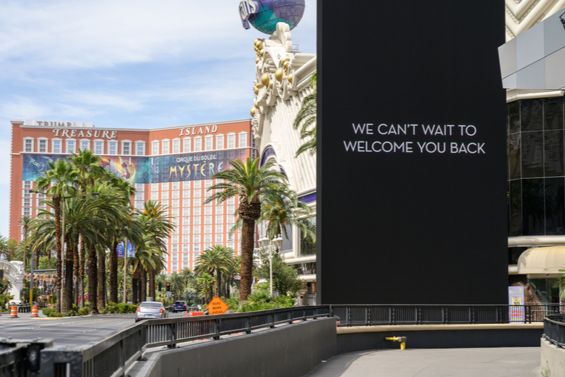 Sign reading "We can't wait to welcome you back" on empty Las Vegas Strip with Treasure Island in background