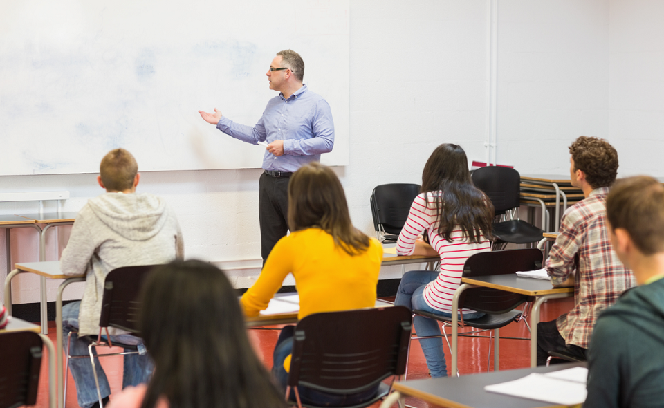 students attentively listening to male teacher in the classroom