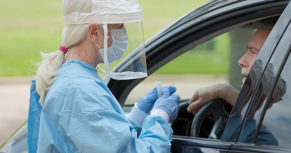 female in medical gear about to conduct a drive-thru swab test on a male patient
