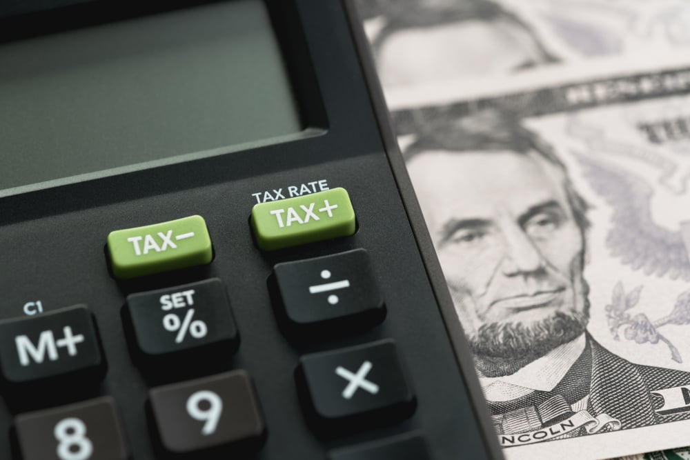 calculator with tax buttons and a US dollar bill in the background