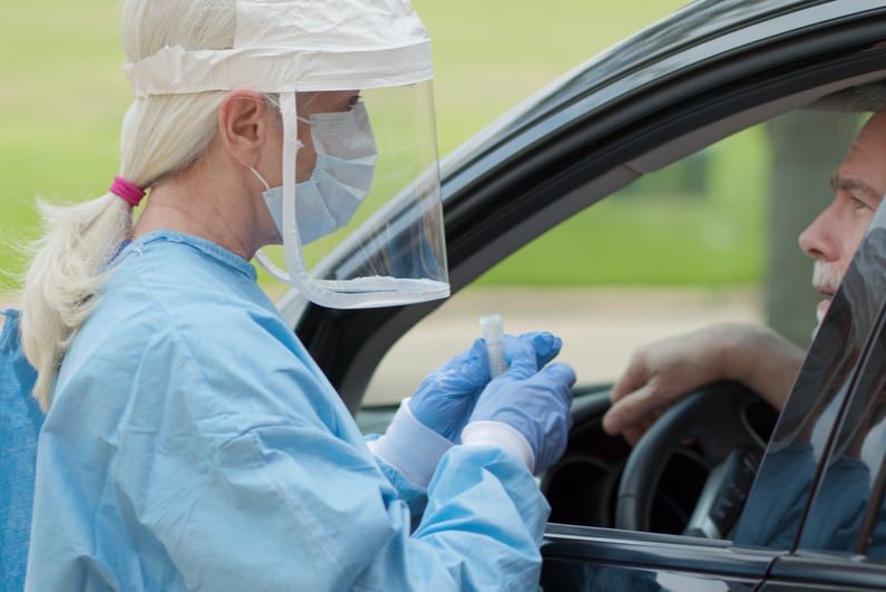 woman with face guard tests a man in a car for coronavirus