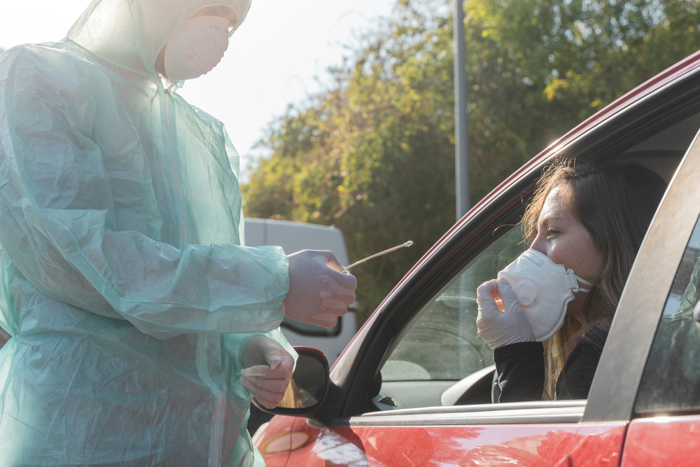 woman in car wearing mask about to be swab tested for coronavirus by a health professional wearing PPE