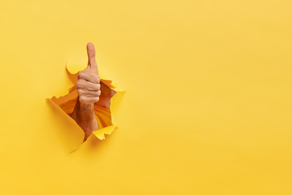 a hand breaking through a yellow wall to indicate a thumbs up