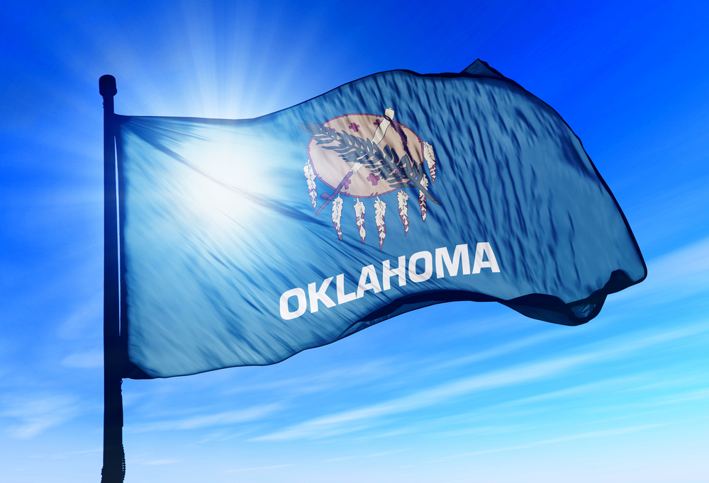 flag of state of Oklahoma against blue sky and sun backdrop