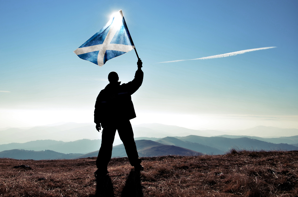silhouette of man standing at the top of Scottish mountains and waving the Scotland flag