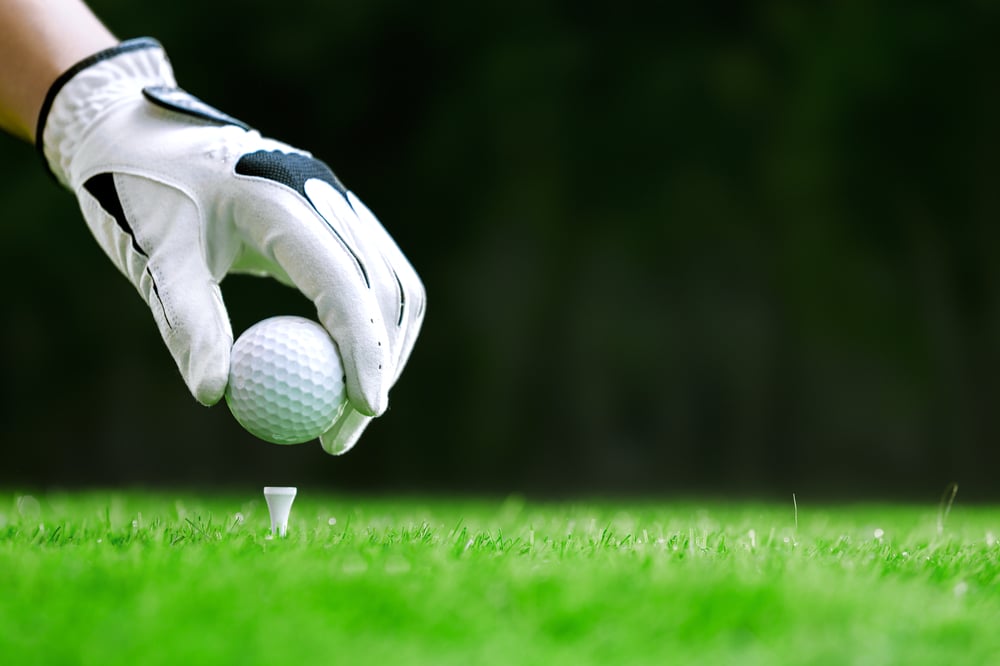 gloved hand placing golf ball on tee on golf course