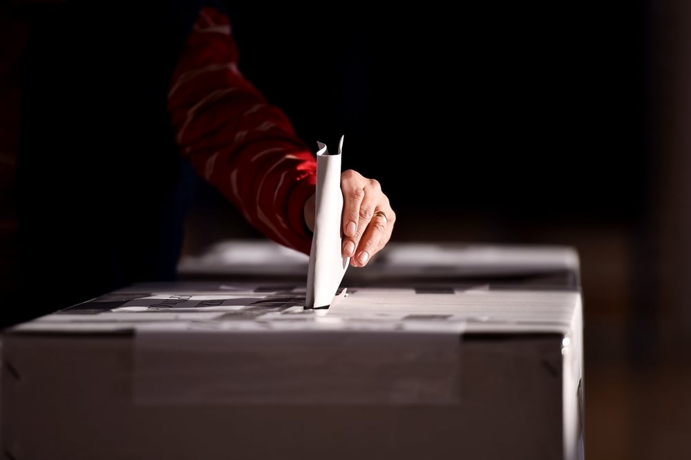 hand casting paper vote in ballot box