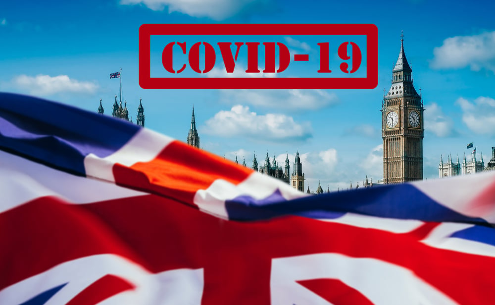 Union Jack flag with Covid-19 stamp above it and the Houses of Parliament building in the background