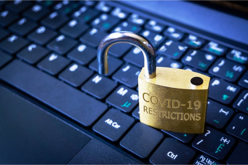 Open padlock stamped with "COVID-19 RESTRICTIONS" on a laptop keyboard