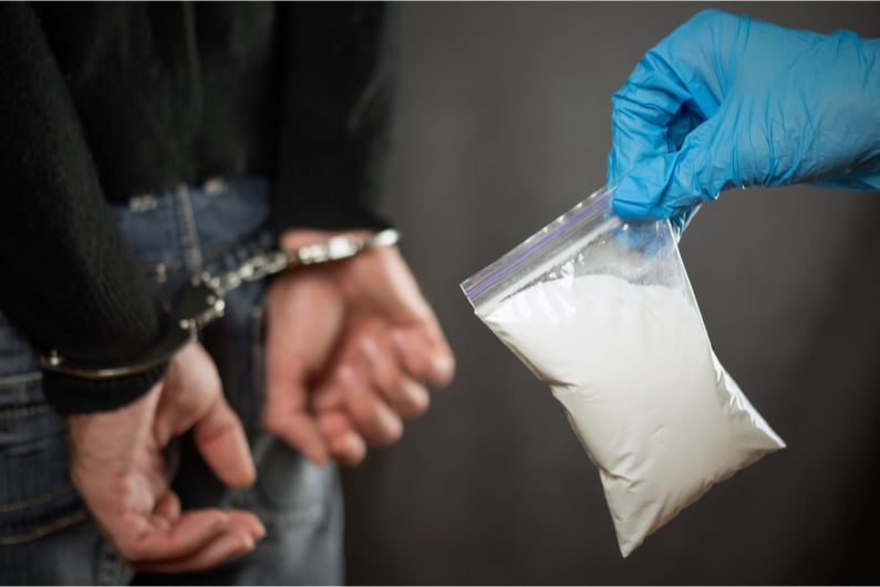 Cop holding a baggie of white powder behind a handcuffed man