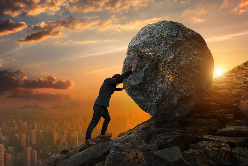 Man pushing boulder up a hill