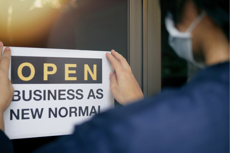 Person hanging "OPEN Business as New Normal" sign on door