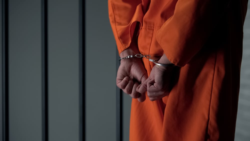 handcuffed man in orange prison jumpsuit behind bars