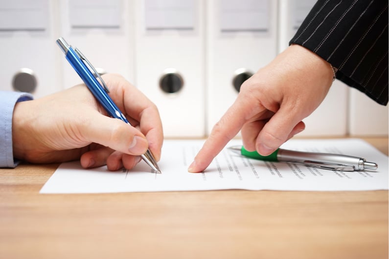 Person signing a document while another points to where to sign