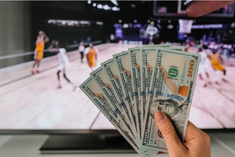 Person holding cash in front of a basketball game on TV