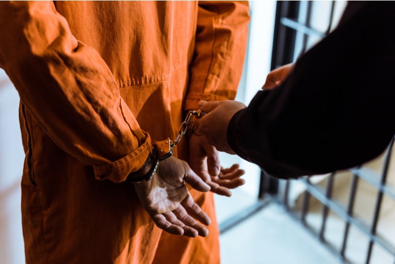 prisoner in orange jumpsuit being cuffed