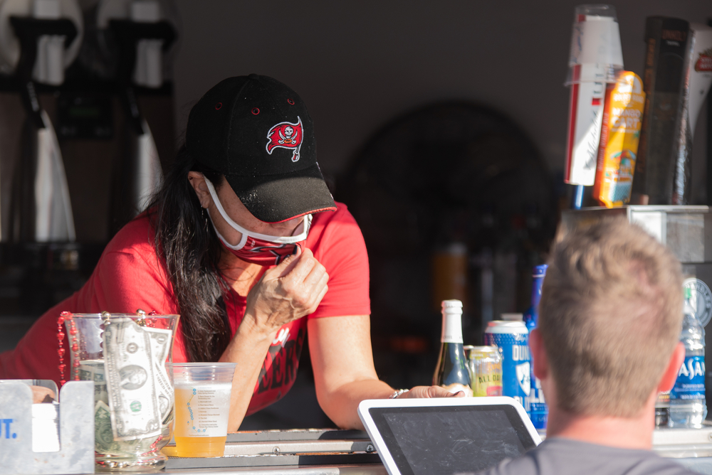 Woman Working in a Food Truck, Wearing a Tampa Bay Buccaneers Hat and face mask in front of customer with tablet