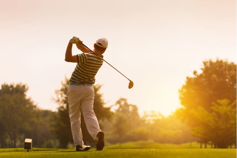 Golfer teeing off at sunset