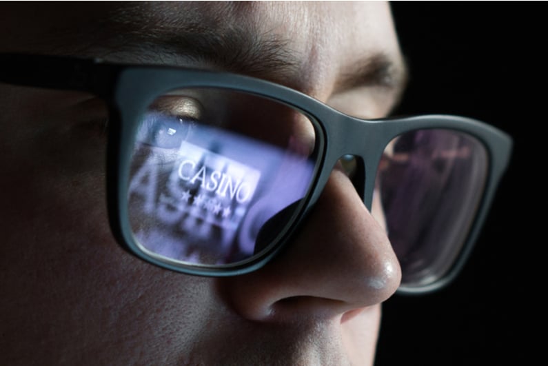 Closeup of man gambling online, the computer screen reflected in his glasses