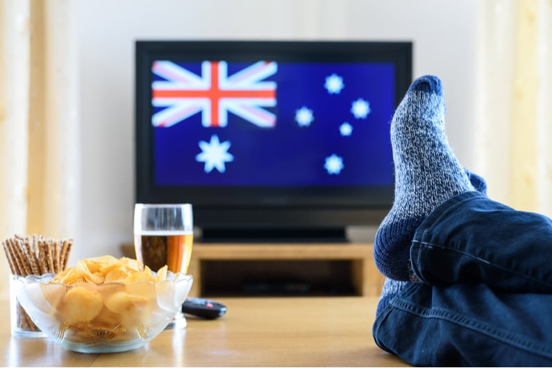 Person with feet propped up on a table with a TV in the background showing the Aussie flag