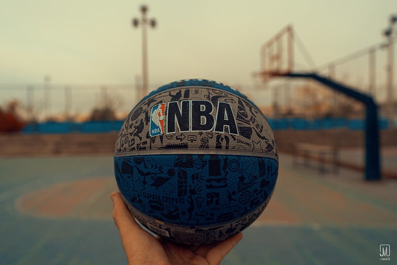 Hand holding NBA logoed blue and grey basketball at an outdoor court