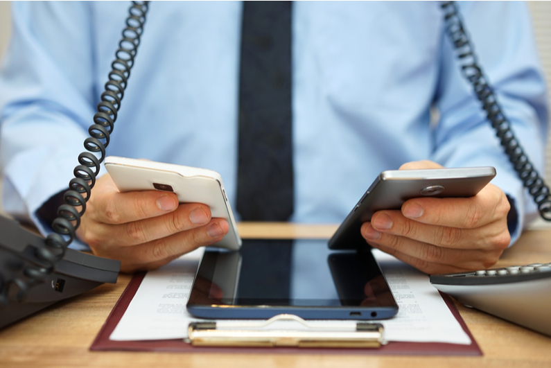 businessman using two cell phones, two corded phones, and a tablet