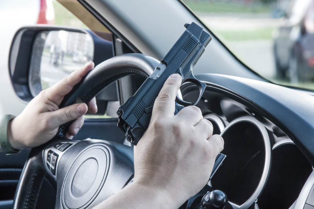 male hands at car steering wheel holding a gun