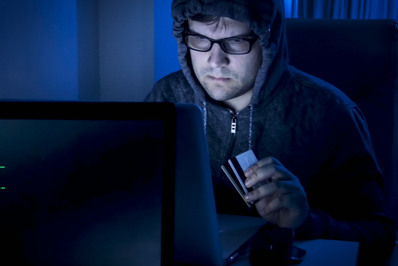 Shady looking guy holding credit cards at computer