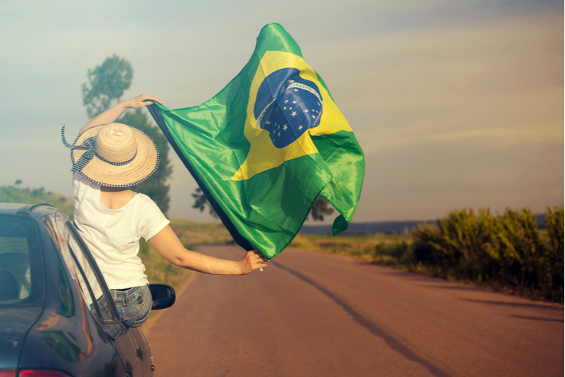 Woman leaning out of a car window flying a Brazil flag