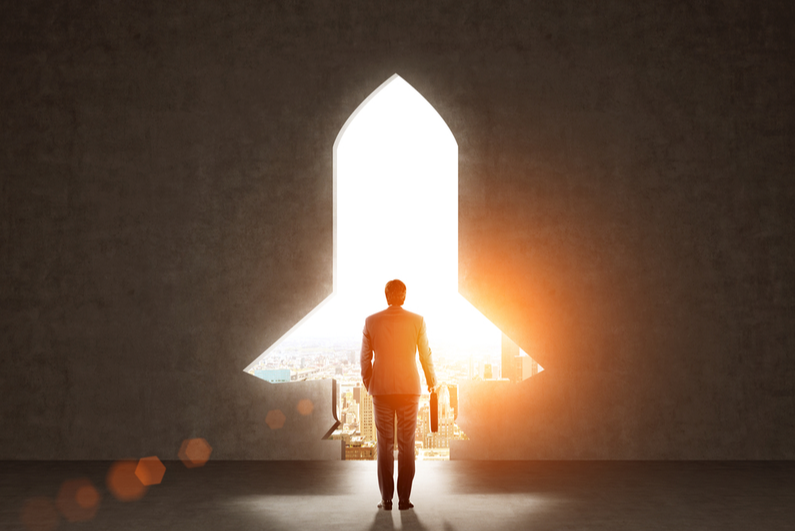 Businessman holding a briefcase standing in front of a brightly-lit, rocket-shaped doorway